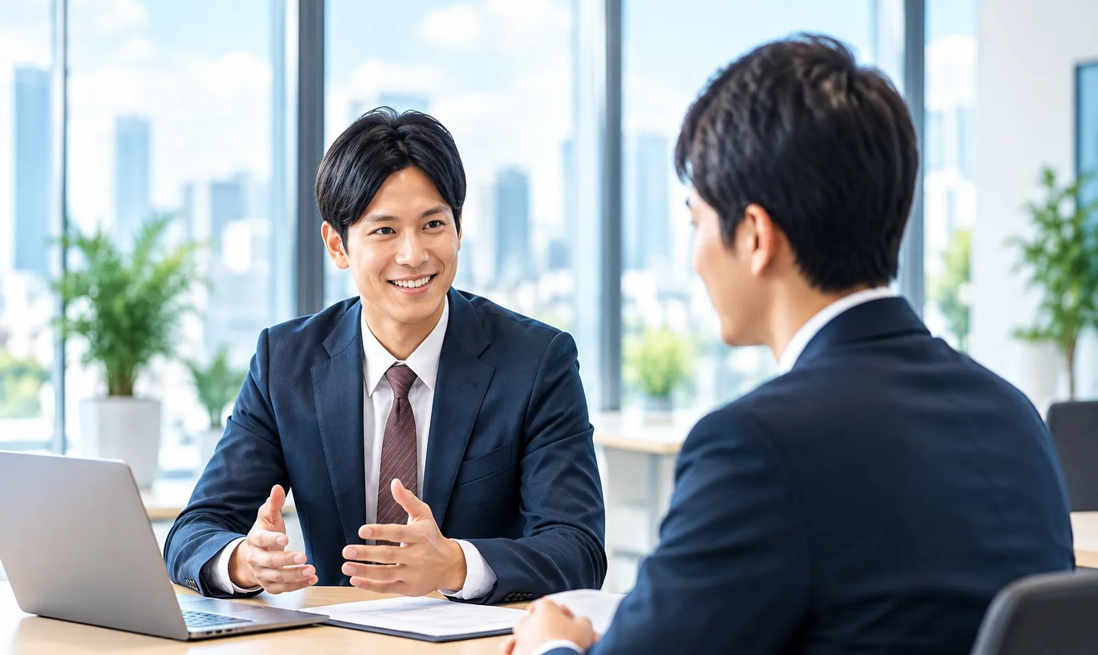 明るいオフィスで、ノートパソコンを前に2人が打ち合わせをしているイメージ画像(AI生成)